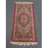 A machine made fringed Persian design rug on red ground,