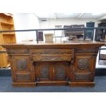 An Arts and Crafts heavily carved oak break front sideboard fitted drawers and cupboards beneath
