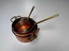 A tray of four brass handled kitchen pots and pans in a copper finish