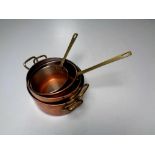 A tray of four brass handled kitchen pots and pans in a copper finish