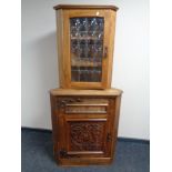 An Arts and Crafts corner cabinet with a carved panel door together with a further wall mounted
