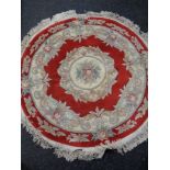 A circular fringed Chinese rug on red ground.