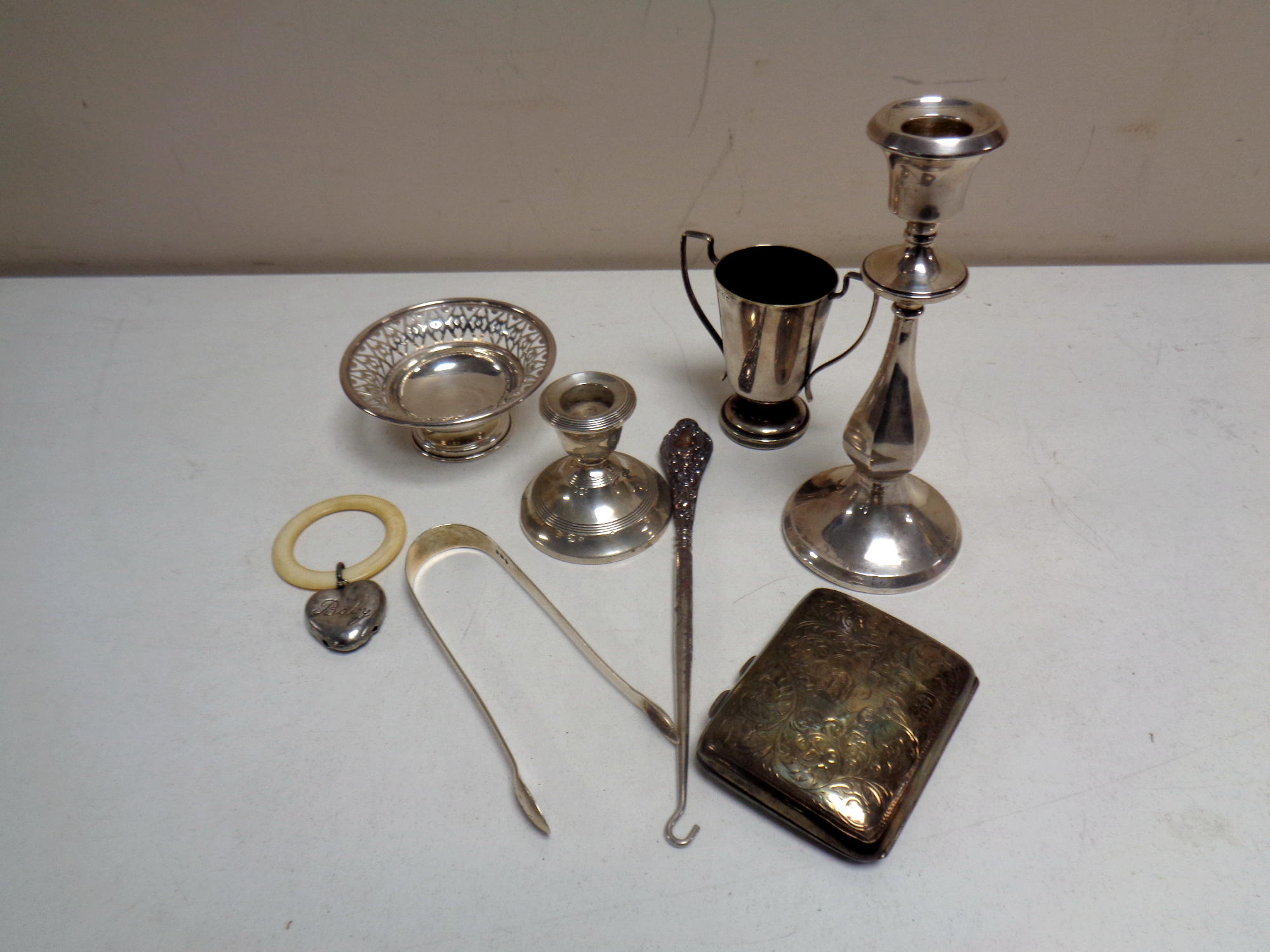 A box containing silver items to include cigarette case, sugar tongs, silver handled button hook,
