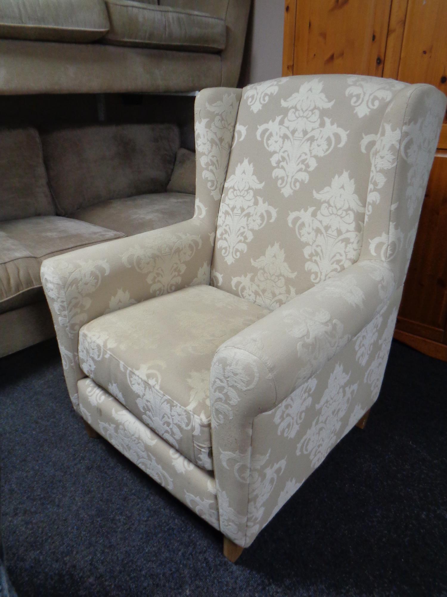 A contemporary high backed wingback armchair upholstered in a cream and beige fabric