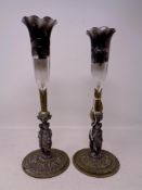 A pair of 19th century figural fluted candlesticks with glass shades on ornate brass bases,