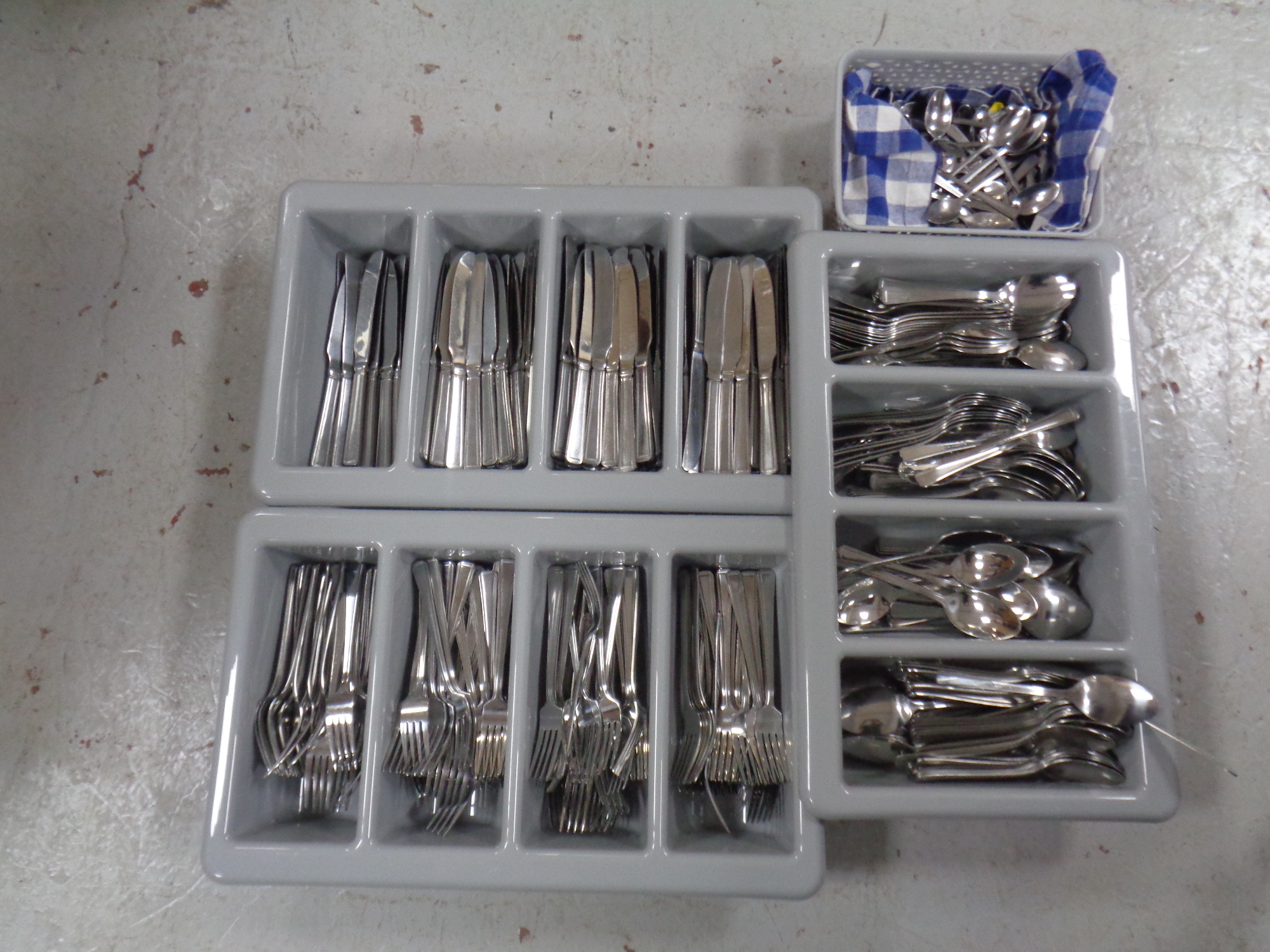 Three cutlery trays and a basket containing a large quantity of stainless steel catering cutlery