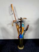 A brass stick stand containing a large quantity of assorted walking sticks, parasol, umbrellas,
