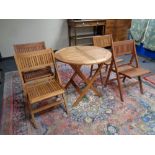 A circular teak garden table and four folding chairs