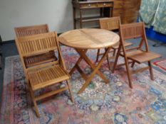 A circular teak garden table and four folding chairs