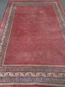 A fringed Persian carpet on red ground 218 cm x 310 cm.