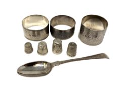 Three various silver napkin rings, a silver spoon and four silver thimbles.