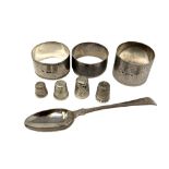 Three various silver napkin rings, a silver spoon and four silver thimbles.