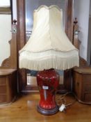 A red ceramic table lamp on wooden base decorated with foliage together with a tasseled shade