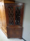 A carved oak corner display cabinet with leaded glass door fitted cupboard beneath