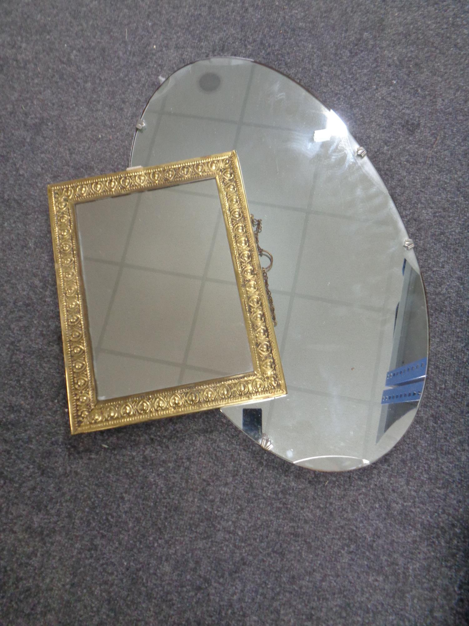 An oval frameless mirror together with a brass embossed framed mirror