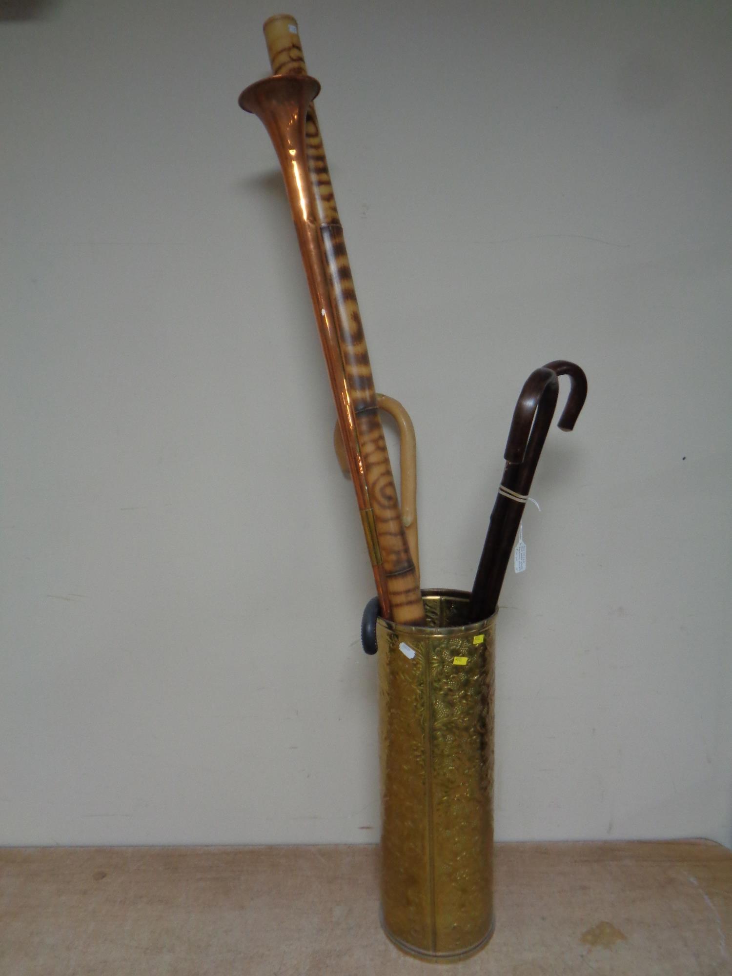 A brass embossed stick stand containing assorted walking sticks, copper and brass horn,