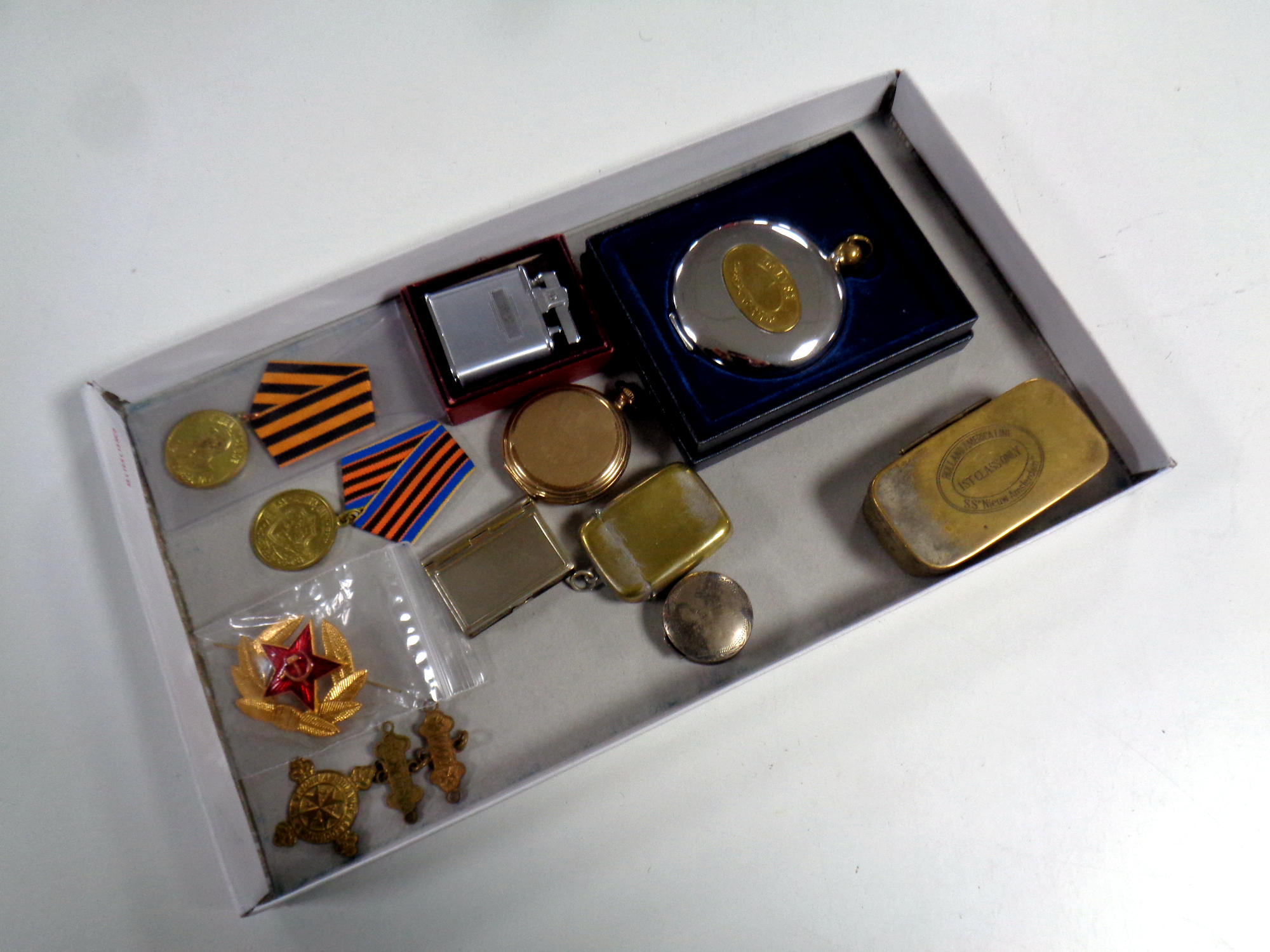 A box of Russian medals and badges, pocket watch, plated vesta case, pocket lighter,