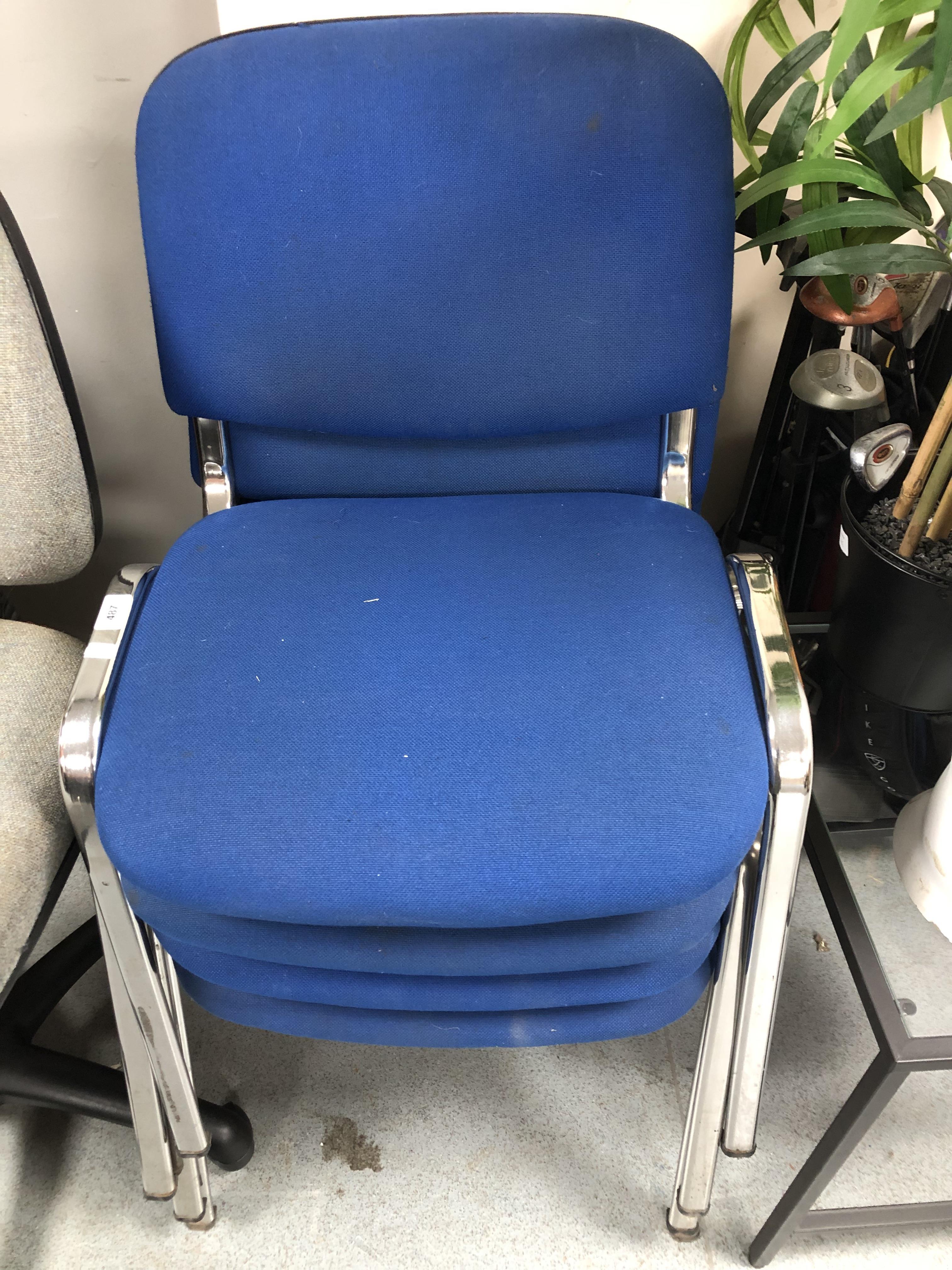 A set of four blue fabric stacking office chairs on metal legs