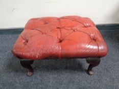 A red button leather Chesterfield footstool on raised legs