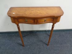 A reproduction walnut shaped hall table fitted two drawers on reeded legs