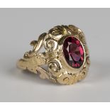 A gold and garnet single stone ring, collet set with an oval cut garnet within a scroll surround,