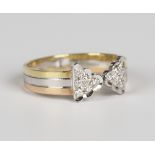 An 18ct three colour gold and diamond ring in a stylized tied ribbon bow design, mounted with