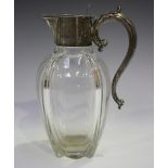 An Edwardian sliver mounted clear glass claret jug with scroll handle and hinged tappit lid,