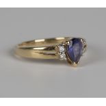 A gold ring, claw set with a pear shaped tanzanite between two pairs of circular cut diamonds,