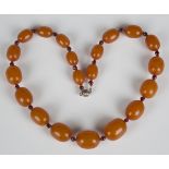 A single row necklace of twenty graduated oval opaque butterscotch coloured amber beads, alternating