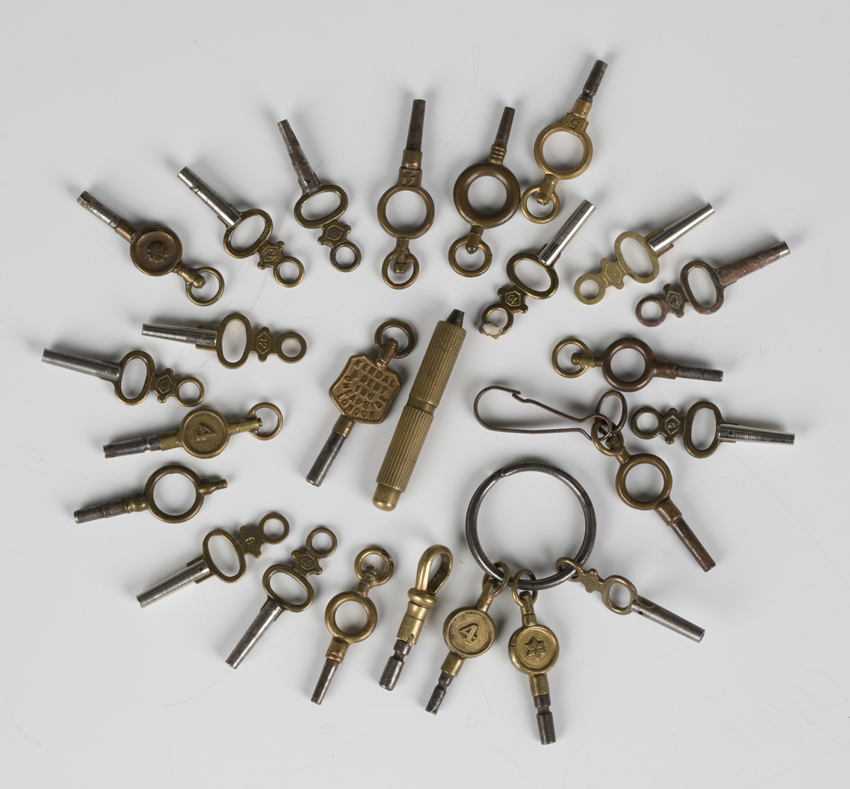 A collection of twenty-five pocket and fob watch keys, including one advertising watch key.Buyer’s