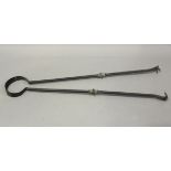 A pair of oversized Arts and Crafts style wrought iron and brass mounted fire tongs, length 123cm.