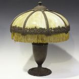 An early 20th century bronzed cast spelter table lamp with a stained glass shade, raised on an ovoid