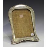 A George V silver photograph frame of shaped rectangular form, embossed with scrolling foliage,
