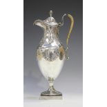 A late Victorian silver hot water jug, the hinged lid with foliate finial above a narrow neck and