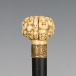 A late 19th century ebonized walking cane, the Japanese ivory handle carved with overall faces,