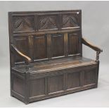 An 18th century provincial oak panelled box seat settle, the back carved with loose lunettes, the