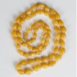 A single row necklace of sixty-nine graduated oval opaque and semi-translucent light honey