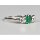 An emerald and diamond three stone ring, mounted with the rectangular step cut emerald between two