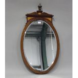 An Edwardian mahogany and satinwood inlaid oval wall mirror with shaped pediment and urn finial,