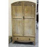 An early 20th century Arts and Crafts style pale oak wardrobe, the arched doors carved with