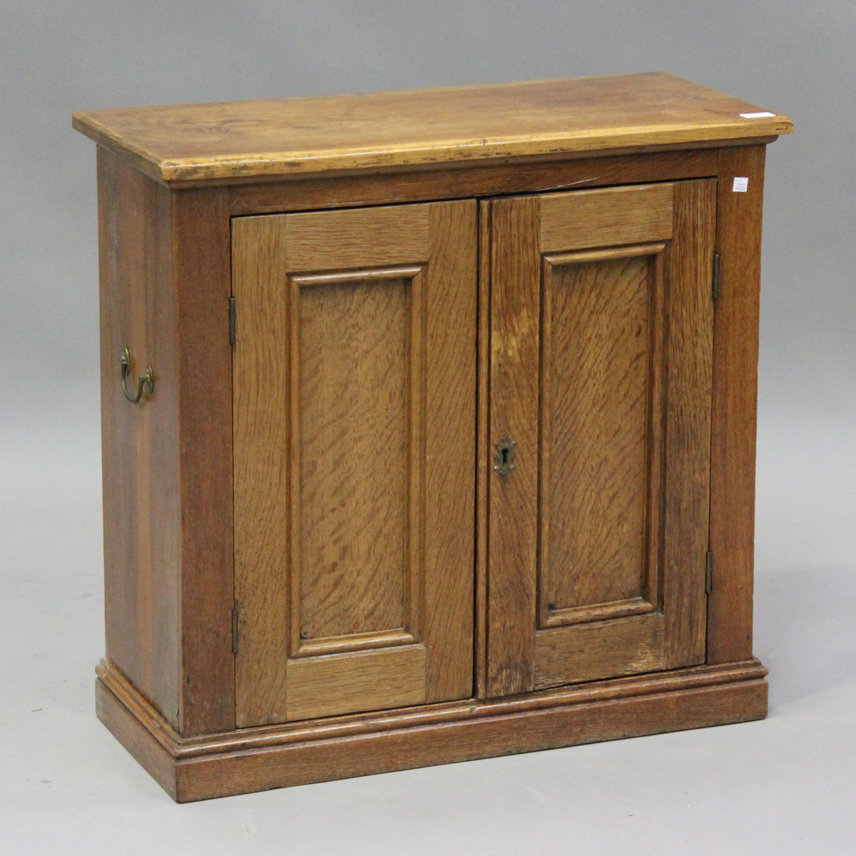 A late 20th century pale oak two-door side cabinet, fitted with carrying handles, on a plinth