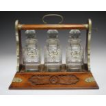An early 20th century oak and plate mounted three-bottle tantalus, fitted with three cut glass
