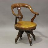 A late Victorian mahogany framed tub back revolving desk chair with a circular brown leather seat,