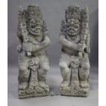 A pair of impressive Balinese carved stone temple statues, each standing figure holding a torch,