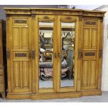 An Edwardian pale oak four-section wardrobe, the doors with carved foliate panels, enclosing sliding