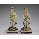 A pair of Staffordshire pearlware putti, first half 19th century, each modelled standing holding a