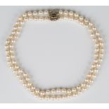 A two row necklace of uniform cultured pearls on a 9ct gold, sapphire and diamond clasp, designed as