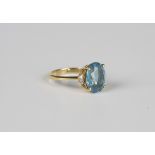 A gold ring, claw set with an oval cut blue topaz between circular cut diamond set two stone