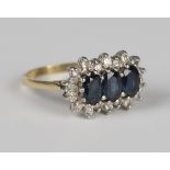 An 18ct gold ring, claw set with three oval cut sapphires within a surround of circular cut