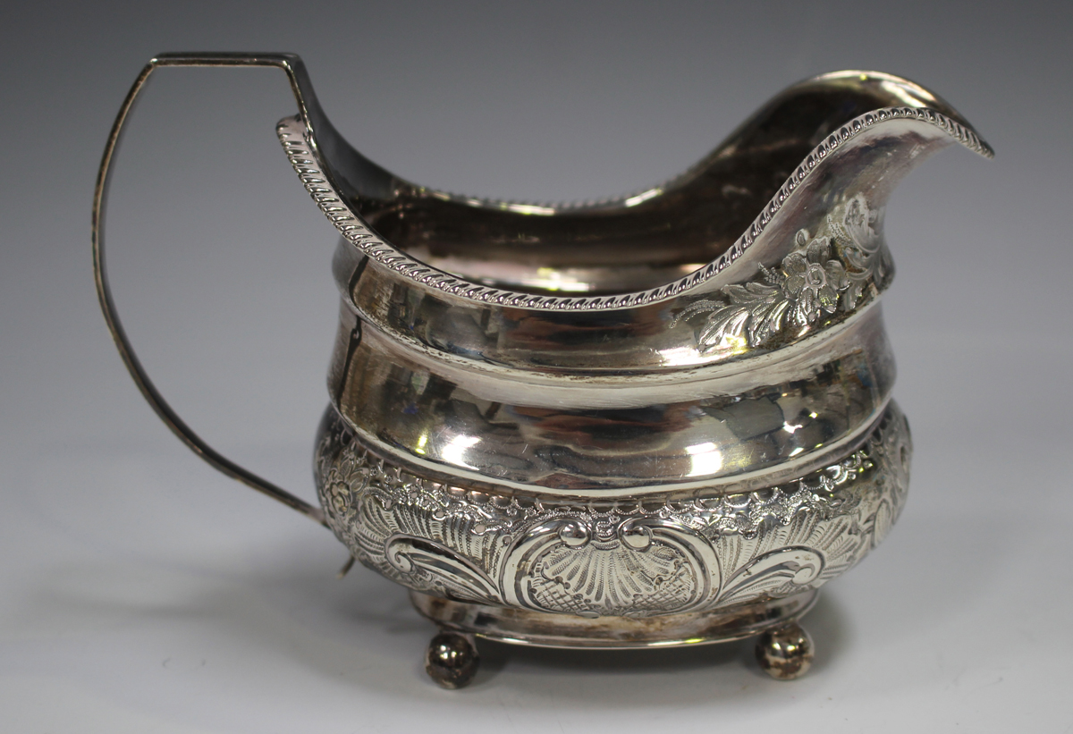 A George III silver cream jug of cushion form with gadrooned rim above a band of foliate scrolls,